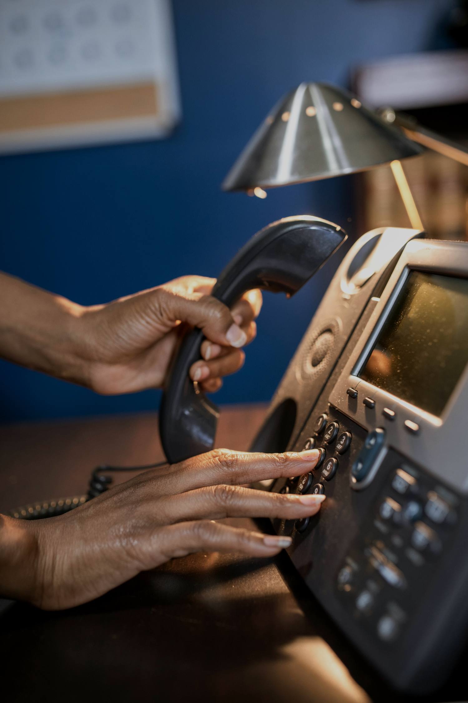A hand dialling a number on a desk telephone keypad.
